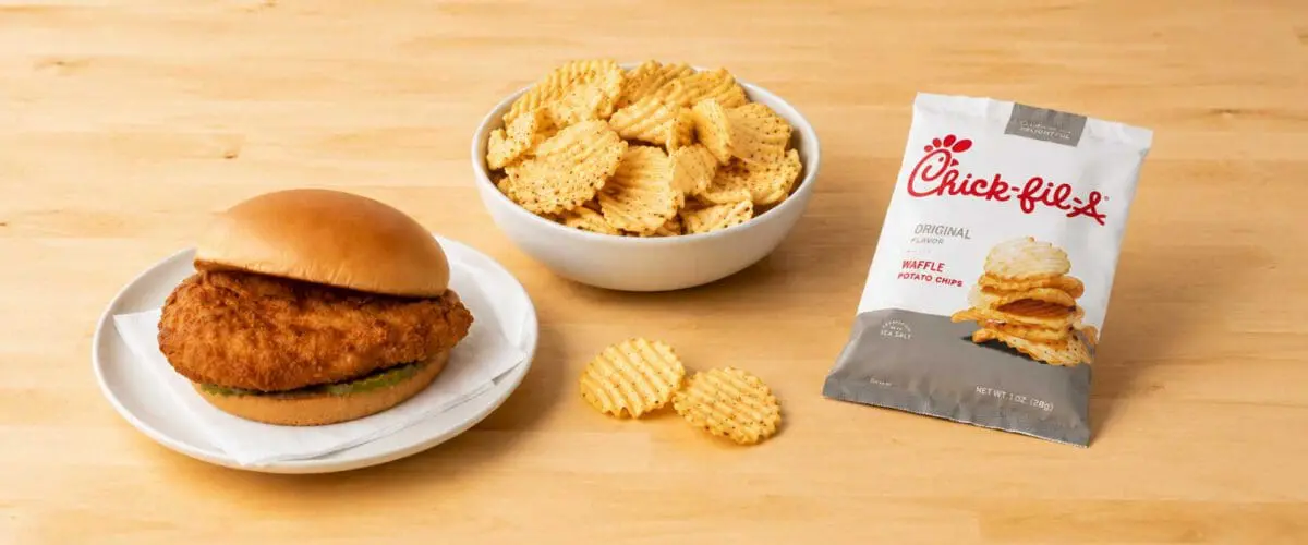 Chicken sandwich and bowl of waffle chips on a wood table