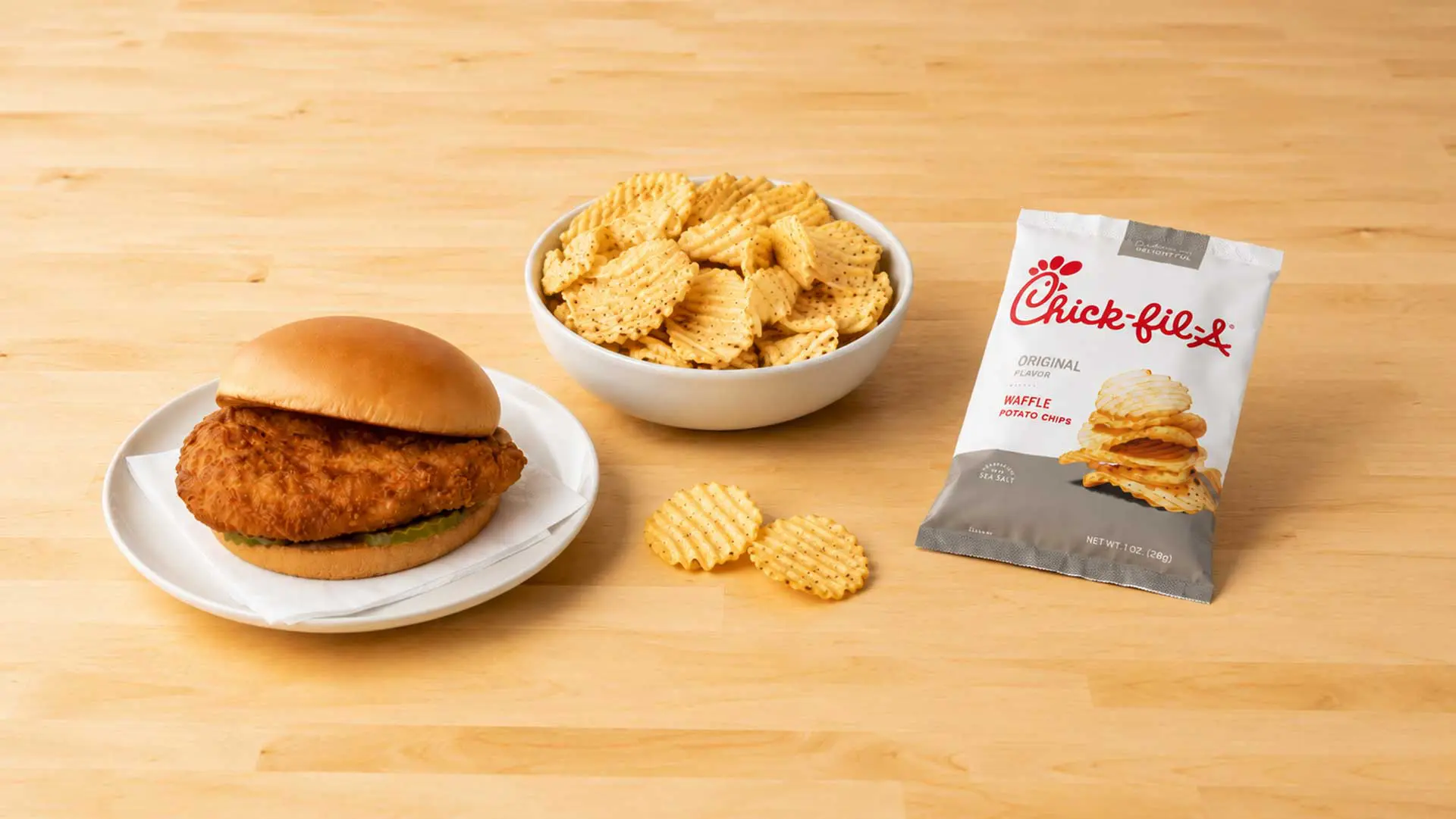 Chicken sandwich and bowl of waffle chips on a wood table