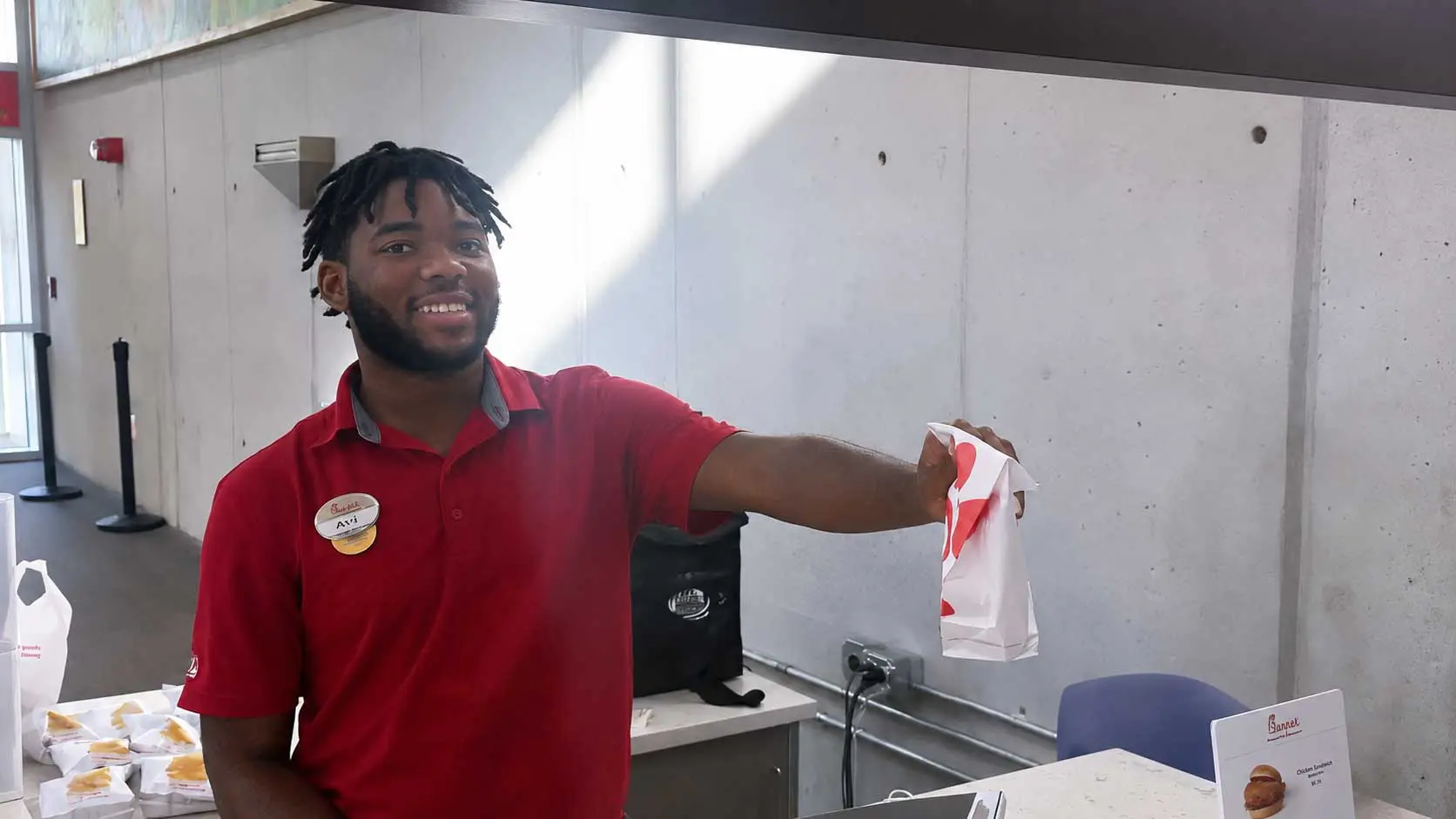 Employee handing a Chick-fil-A paper bag over counter while smiling